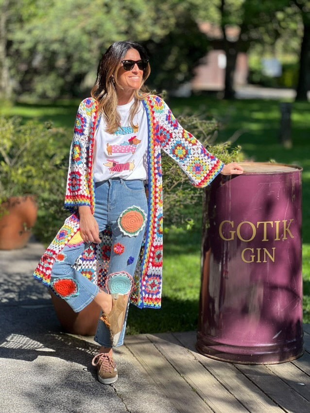 Casaco/kimono comprido de crochet GRINE com padrão colorido e ponto aberto, usado por uma mulher com calças de ganga decoradas.