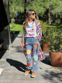 Casaco/kimono comprido de crochet GRINE com padrão colorido e ponto aberto, usado sobre t-shirt branca e calças de ganga com aplicações de crochet.