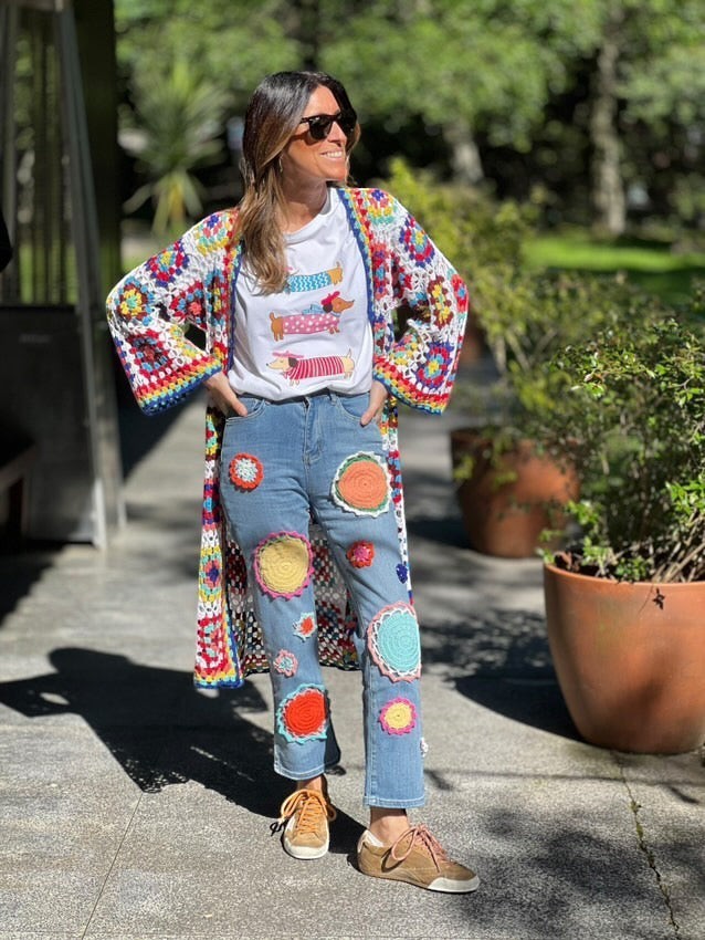 Casaco/kimono comprido de crochet GRINE com padrão colorido e ponto aberto, usado por uma mulher com calças de ganga decoradas com aplicações de crochet.