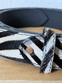 Cinto GRINE de couro com padrão de pelo de zebra em preto e branco, detalhe de rebite metálico e 3,5 cm de largura.