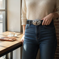 Cinto GRINE de couro preto com fivela prateada em forma de chifre, usado por mulher com jeans e camisola bege.