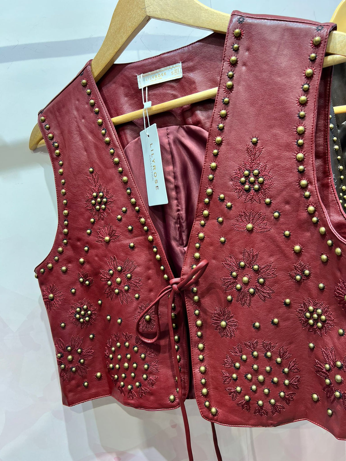 Colete GRINE Chester em PU bordeaux com bordados florais e tachas metálicas, fechado com atilho frontal.