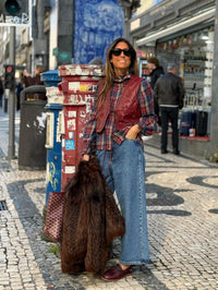 Mulher usa colete GRINE Chester em PU bordeaux com tachas e bordados sobre camisa xadrez em ambiente urbano