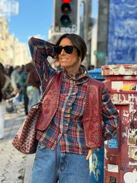 Mulher a usar colete GRINE Chester em PU bordeaux com bordados e tachas sobre camisa de xadrez em ambiente urbano