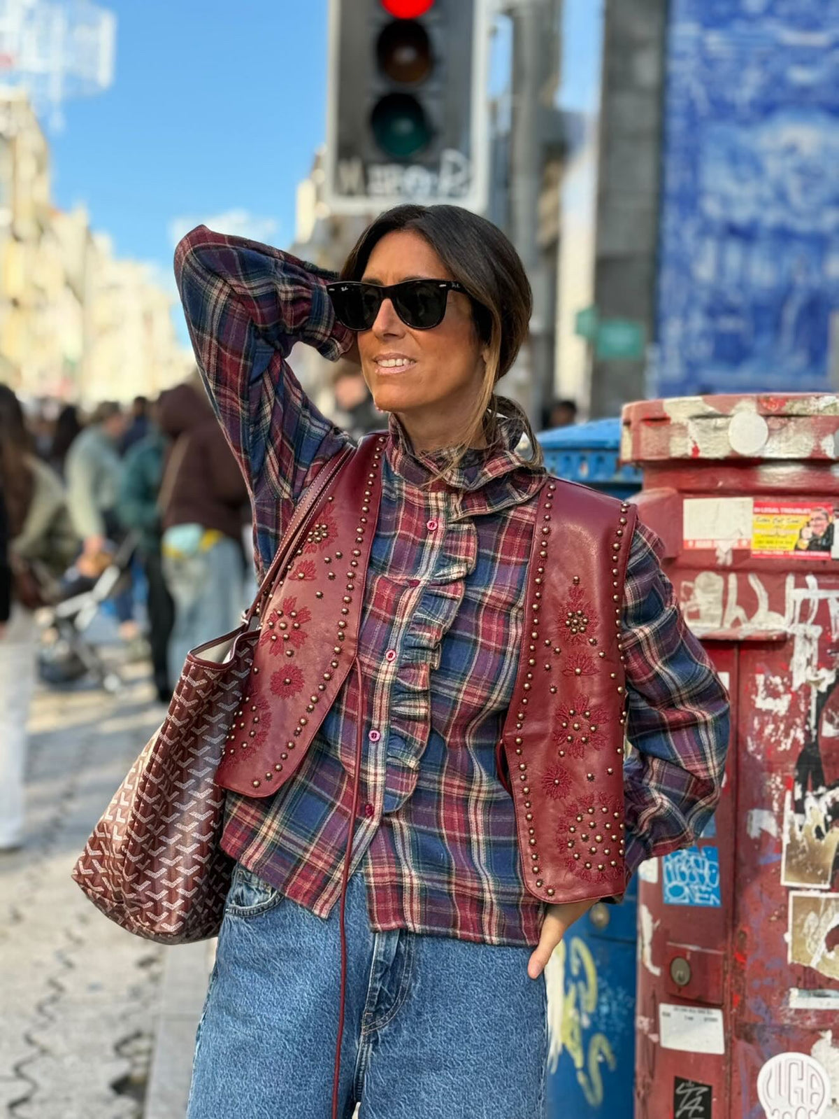 Mulher a usar colete GRINE Chester em PU bordeaux com bordados e tachas sobre camisa de xadrez em ambiente urbano