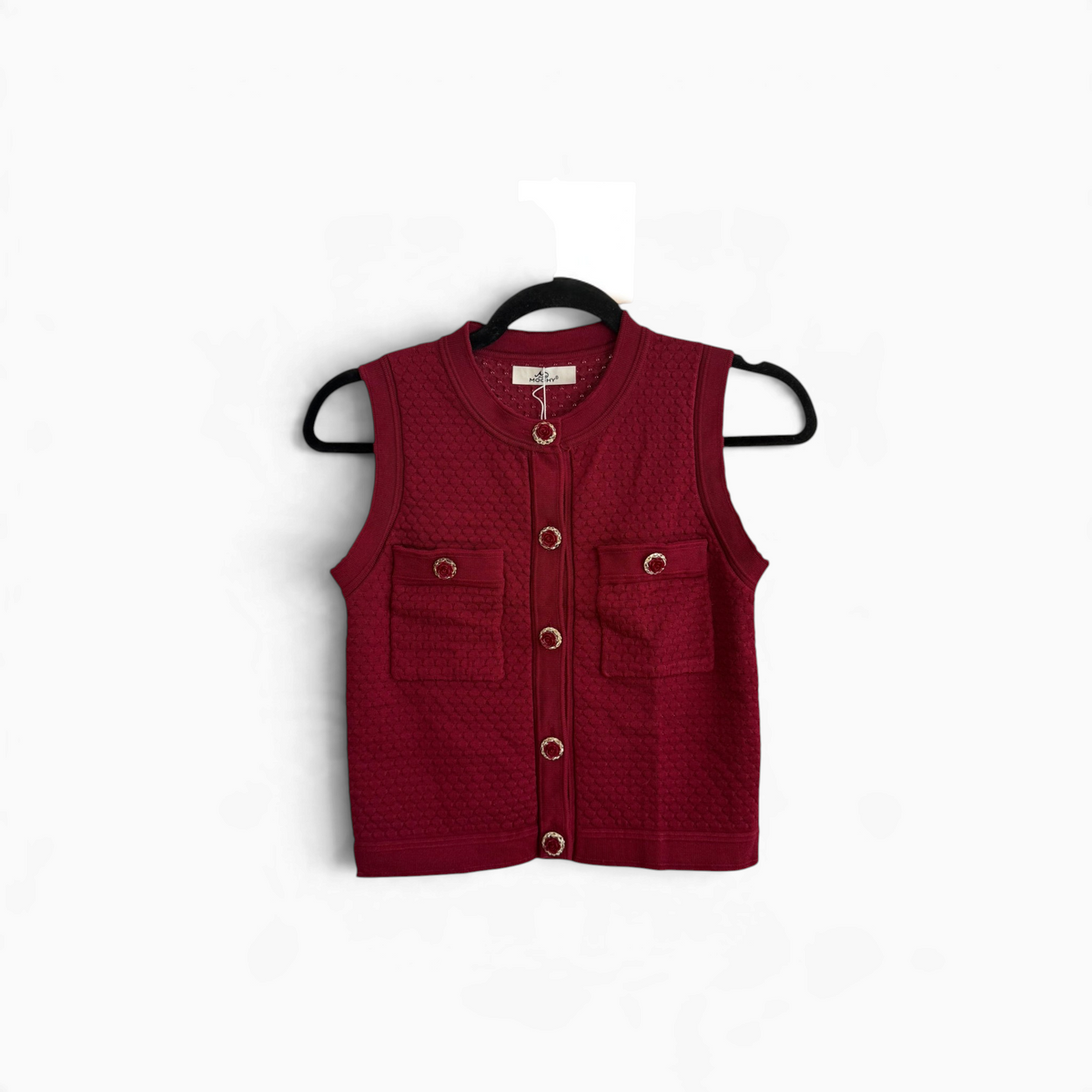 Colete de malha GRINE bordeaux com textura acolchoada, botões trabalhados e bolsos frontais, pendurado num cabide.