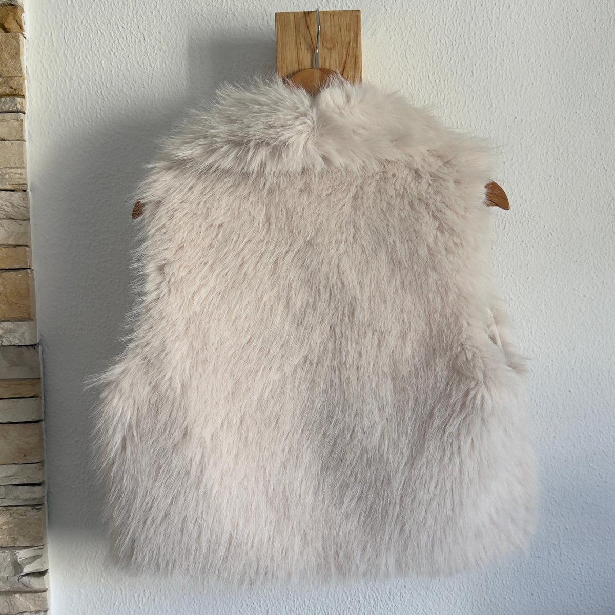 Colete de pêlo sintético bege GRINE, peça elegante e quente para looks sofisticados, pendurado em cabide de madeira.