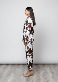 Modelo de perfil vestindo conjunto GRINE de blazer e calças com estampa cow castanha e branca em tecido estruturado