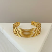 GRINE gold-tone stainless steel cuff bracelet with a multi-layered openwork design. Adjustable and water-resistant.