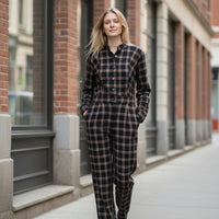 Modelo veste jardineiras GRINE pretas em algodão com padrão xadrez, corte direito e bolsos, em ambiente urbano.