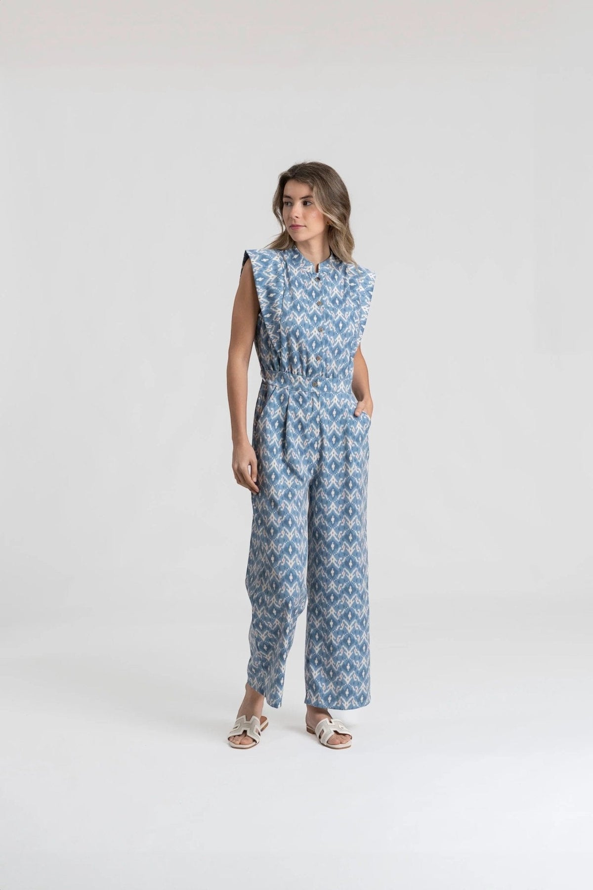 Modelo veste jardineiras azuis GRINE com padrão geométrico, corte direito, bolsos laterais e cintura com elástico.