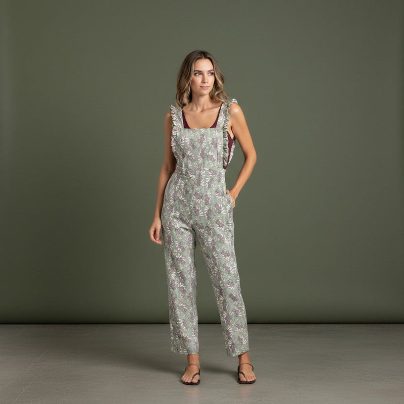 Jardineiras GRINE verdes com padrão floral, corte direito, alças com folhos e bolsos laterais em modelo feminino.