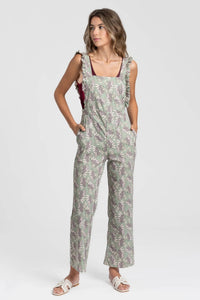 Modelo veste jardineiras GRINE verdes com padrão floral, corte direito, folhos nas alças e bolsos laterais.