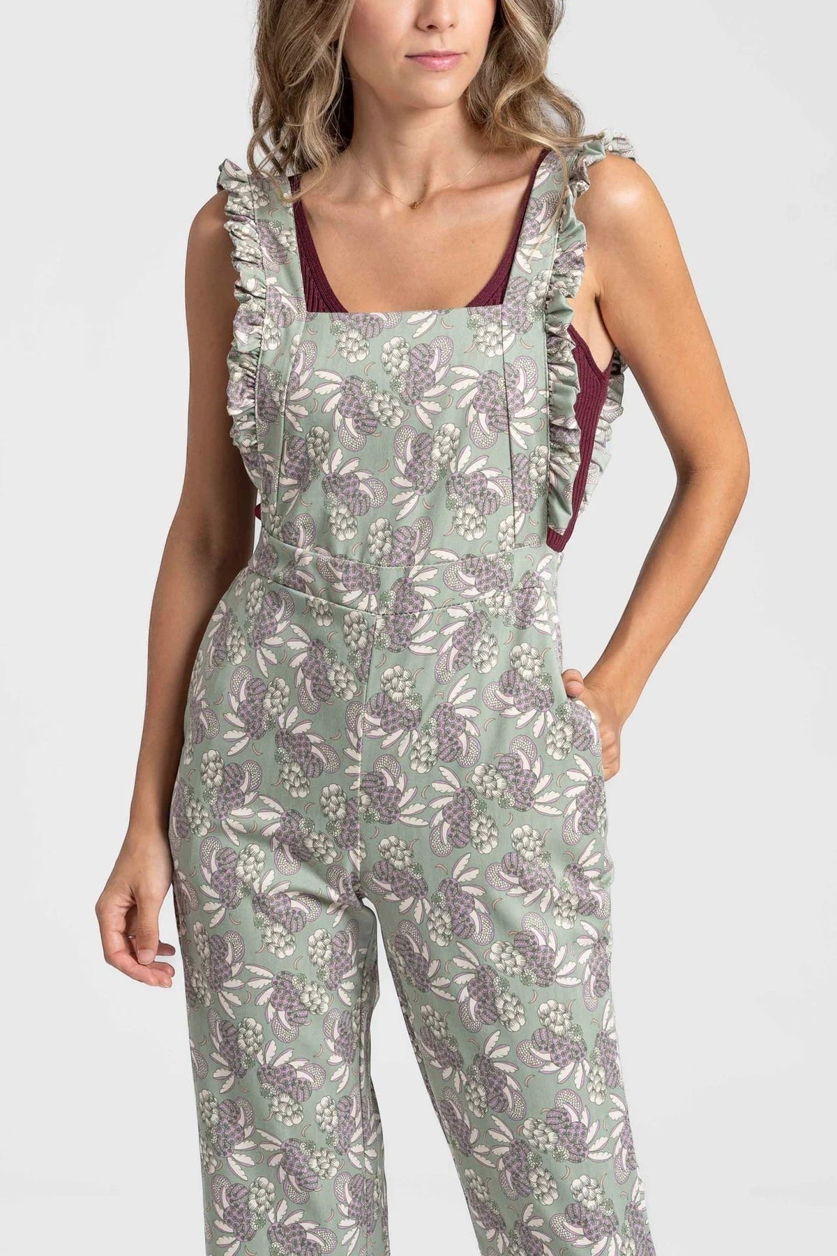 Jardineiras GRINE verdes com padrão floral, alças com folhos e corte direito, vestidas por uma modelo.