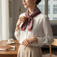 Mulher usa lenço quadrado acetinado GRINE na cor bordeaux com padrão paisley atado ao pescoço sobre camisa branca