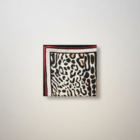 Lenço quadrado GRINE acetinado com padrão animal print em tons de preto, bege e detalhe de linha vermelha.