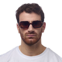 Homem a usar óculos de sol GRINE OKKIA ANDREA com armação em acetato castanho havana e lentes degradé polarizadas.