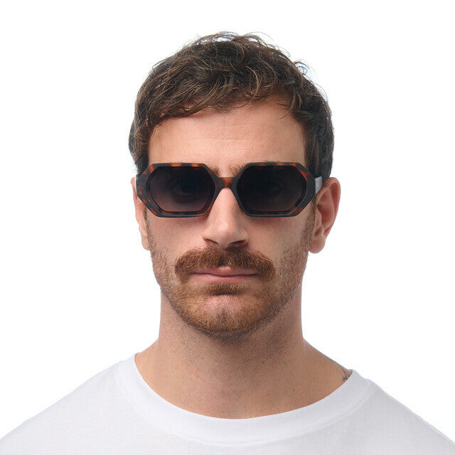 Homem a usar óculos de sol GRINE OKKIA ANDREA com armação hexagonal padrão Havana e lentes verdes degradé