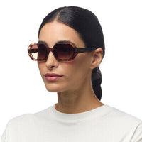 Mulher a usar óculos de sol OKKIA ANDREA com armação em acetato padrão havana e lentes castanhas degradé polarizadas.