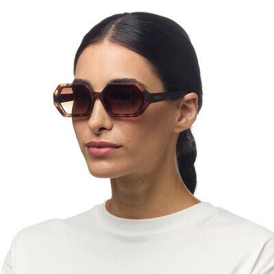Mulher a usar óculos de sol OKKIA ANDREA com armação em acetato padrão havana e lentes castanhas degradé polarizadas.