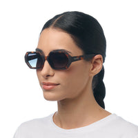 Modelo usa óculos de sol GRINE OKKIA ANDREA com armação hexagonal Havana clássico e lentes verdes em degradé.
