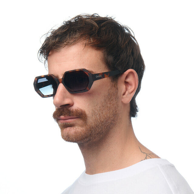 Homem a usar óculos de sol GRINE OKKIA ANDREA com armação hexagonal padrão Havana e lentes verdes em degradé