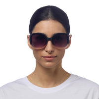 Mulher usando óculos de sol GRINE OKKIA ANNA com armação preta e rosa e lentes degradê polarizadas