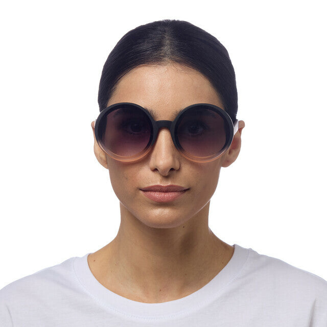 Mulher a usar óculos de sol redondos GRINE OKKIA Monica com armação preta e lentes degradé rosa e pretas