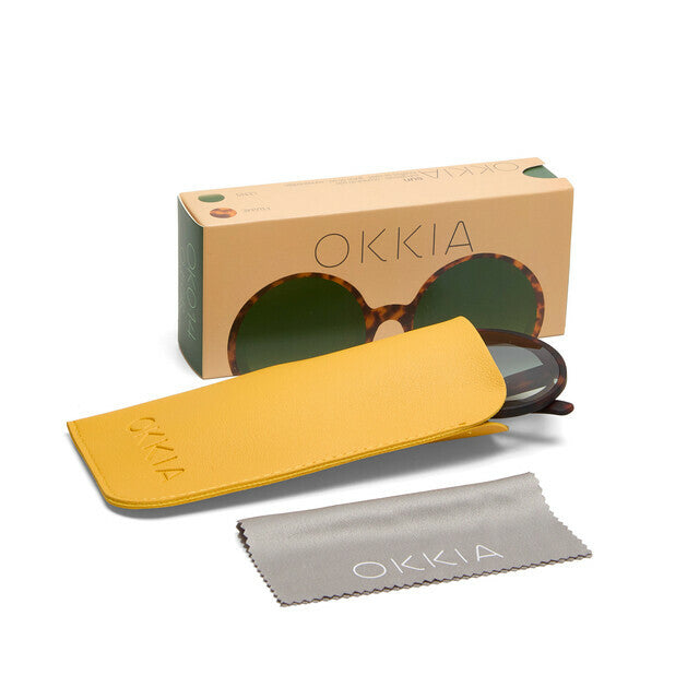 Óculos de sol GRINE OKKIA Monica redondos com armação tartaruga, lentes verdes, estojo amarelo e pano de limpeza.