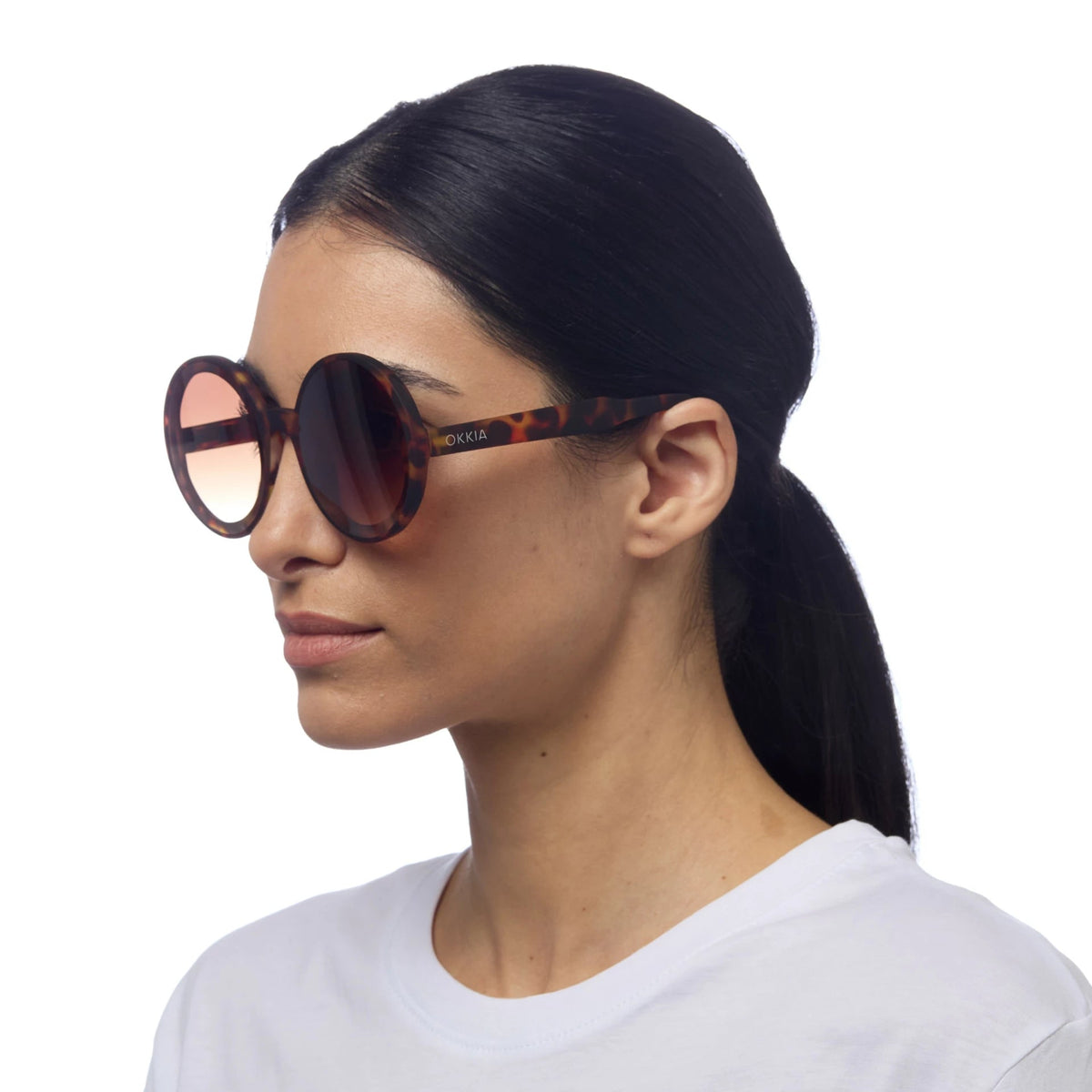 Mulher a usar óculos de sol redondos OKKIA MONICA com armação tartaruga e lentes castanhas, vendidos pela GRINE.