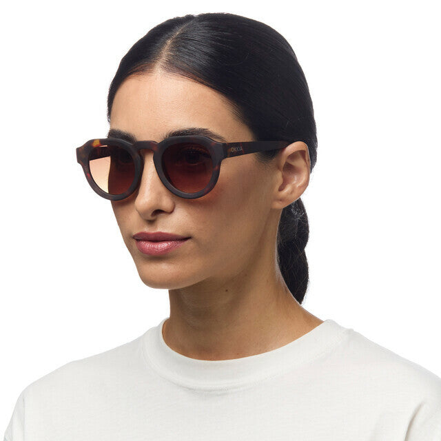 Mulher a usar óculos de sol GRINE OKKIA ZENO com armação Classic Havana e lentes castanhas polarizadas