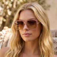 Mulher loira a usar óculos de sol GRINE OKKIA Alessia com armação quadrada Pink Havana e lentes castanhas degradé