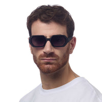 Homem a usar óculos de sol GRINE OKKIA ANDREA com armação hexagonal preta e lentes degradé de toque suave