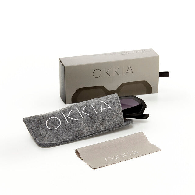 Óculos de sol GRINE OKKIA ANDREA pretos com armação hexagonal, bolsa de feltro cinzenta, caixa e pano de limpeza.
