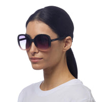 Mulher a usar óculos de sol GRINE OKKIA ANNA com armação preta e lentes degradé rosa, design elegante e feminino.