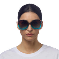 Mulher a usar óculos de sol GRINE OKKIA ANNA com armação tartaruga e azul e lentes castanhas degradé polarizadas