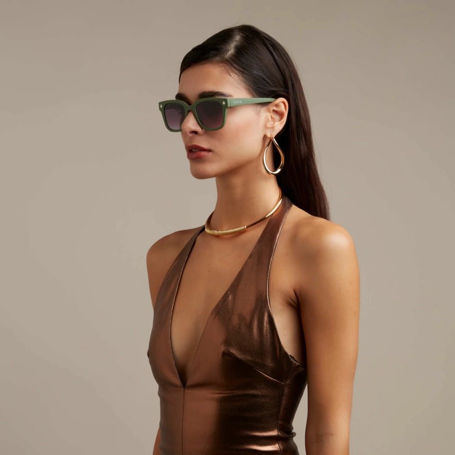 Modelo usa óculos de sol GRINE OKKIA Giovanni com armação verde e preta em acetato e lentes polarizadas pretas.