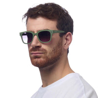 Homem a usar óculos de sol GRINE OKKIA Giovanni com armação verde e preta em acetato e lentes polarizadas pretas.