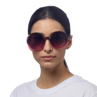 Mulher a usar óculos de sol redondos GRINE OKKIA Monica com armação tartaruga e rosa e lentes castanhas polarizadas