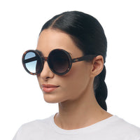 Mulher a usar óculos de sol redondos GRINE OKKIA Monica com armação tartaruga e lentes verdes polarizadas