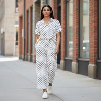 GRINE pearl white cotton short-sleeve shirt with black polka dots and side slits, paired with matching wide-leg trousers.