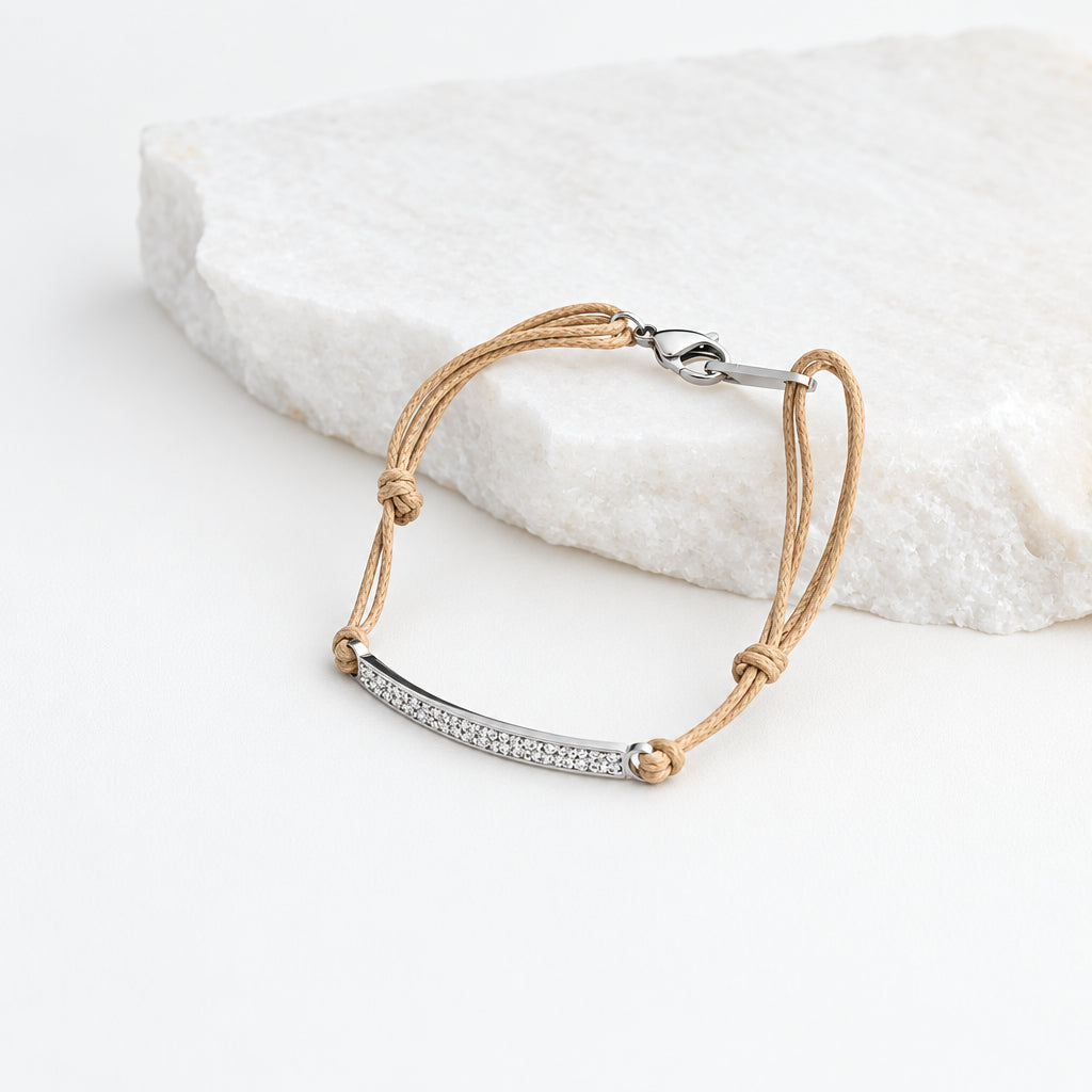 Pulseira GRINE ajustável em aço inoxidável prateado com detalhes brilhantes e cordão bege sobre pedra branca