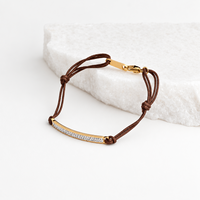Pulseira GRINE ajustável com barra de aço inoxidável dourada, detalhes brilhantes e cordão castanho sobre pedra