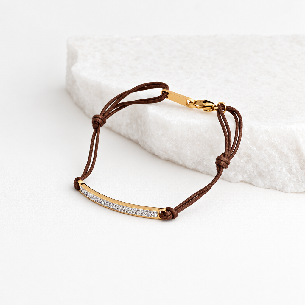 Pulseira GRINE ajustável com barra de aço inoxidável dourada, detalhes brilhantes e cordão castanho sobre pedra