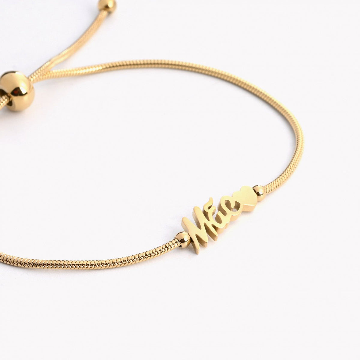 Pulseira ajustável GRINE em aço inoxidável dourado com a palavra Mãe e um pequeno coração em detalhe.