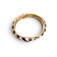 Pulseira rígida GRINE com padrão geométrico em esmalte preto e branco sobre base dourada e fecho de mola.