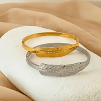 Pulseira Leaf GRINE em aço inoxidável dourado e prateado com detalhes em strass sobre suporte branco e tecido bege