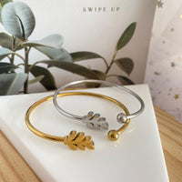 Pulseira rígida GRINE Leaf em aço inoxidável prateado e dourado com detalhe de folha sobre base triangular branca