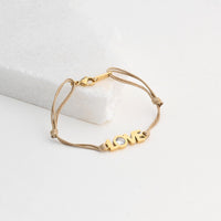 Pulseira GRINE LOVE em aço inoxidável bege com detalhe brilhante e fecho ajustável sobre base branca