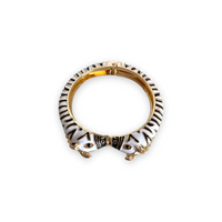 Pulseira rígida GRINE com padrão zebra em esmalte preto e branco, feita em cobre com abertura de mola.